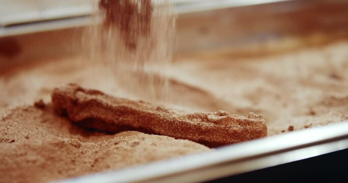 coating churro with sugar + cinnamon with metal tongs in festival booth