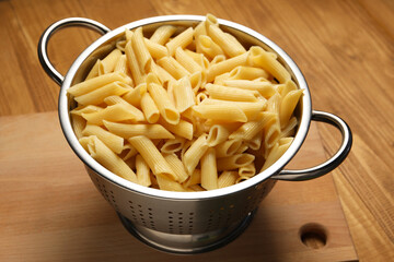 Cooked pasta in metal colander on wooden table, closeup