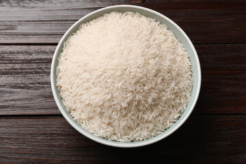 Raw basmati rice in bowl on wooden table, top view