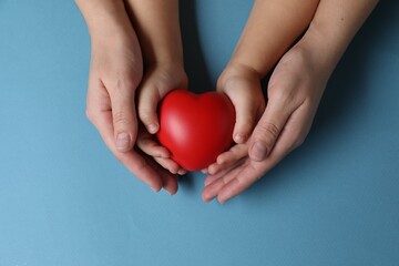 Mother and her child holding red decorative heart on light blue background, top view