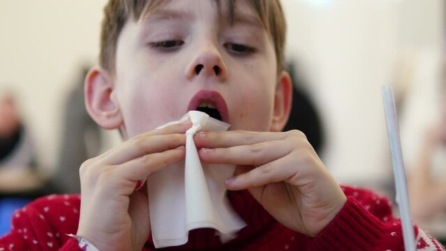 Little gentleman in a cafe: with a sophisticated gesture, a Caucasian boy of 9 years old wipes his mouth and hands after a delicious lunch. Cleanliness and etiquette concept