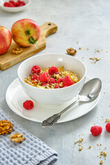 Oat porridge with apples and fresh raspberries in a white cup on a gray background.
