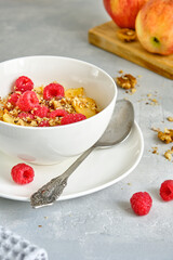 Oat porridge with apples and fresh raspberries in a white cup on a gray background.