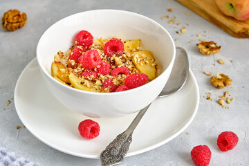 Oat porridge with apples and fresh raspberries in a white cup on a gray background.