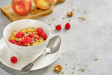 Oat porridge with apples and fresh raspberries in a white cup on a gray background.