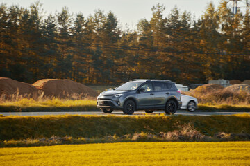 A hybrid SUV car journeys along a scenic road with majestic nature and a golden sunset in the...