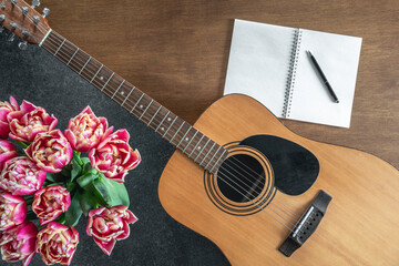 Top view, acoustic guitar, notepad and tulips on the table.