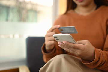 Young woman holding credit card and using mobile phone. Banking transaction and shopping online concept