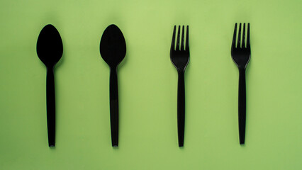 Black plastic spoon and fork isolated on green background