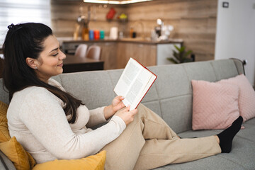 Woman reading a book while relaxing on a sofa at home