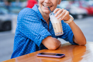 Caucasian woman drinking iced coffee on the outdoor terrace of a cafe on a hot summer day.