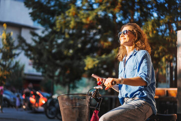 A young Caucasian woman using a smartphone while standing next to her bicycle in the summer city street. - 746384333