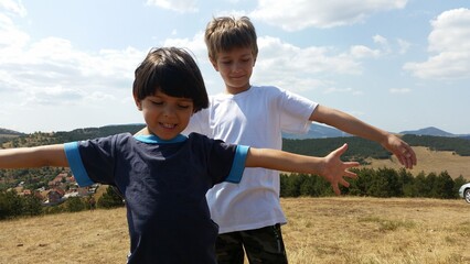 Happy kids standing on the green field with hands wise, on the Sunny day. Boys Summer photo. Landscape mountain 