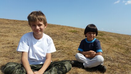 Happy kids sitting on the green field, on the Sunny day.. Boys Summer photo. Landscape mountain 