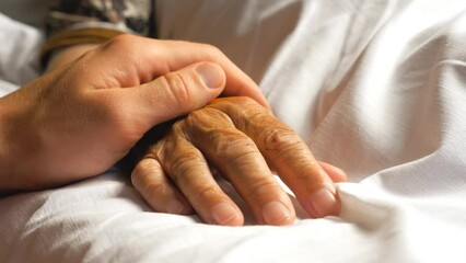 Unrecognizable worried man gently stroking hand of his sick grandmother giving support. Son comforting wrinkled arm of elderly mom lying at bed in hospital. Guy showing care or love to old parent