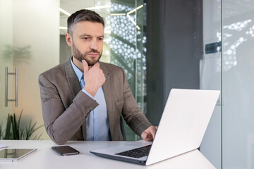 Naklejka premium Thoughtful business professional analyzing data on laptop in modern office setting