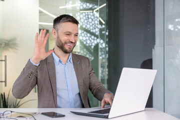 Fototapeta premium Friendly businessman waving hand during a video call on laptop at office
