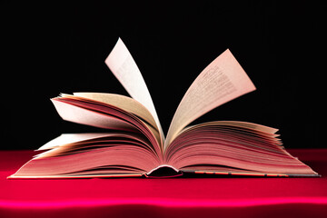 Pages of a thick book are turned on a pink and black background