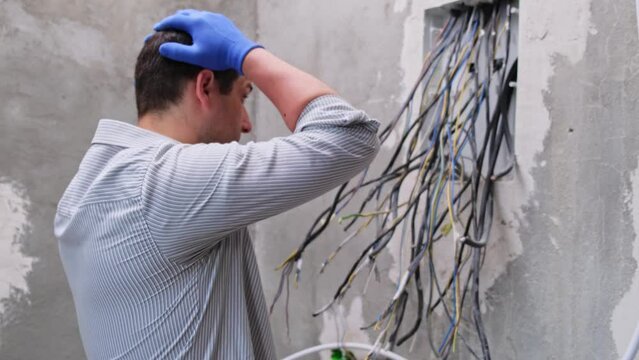 young Male electrician perplexed dumbfounded installing cables and wires in a new electrical enclosure