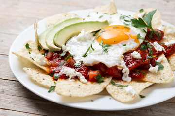 Fototapeta na wymiar Traditional Mexican breakfast red chilaquiles with egg on wooden table. Close up