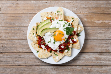Traditional Mexican breakfast red chilaquiles with egg on wooden table