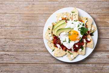 Traditional Mexican breakfast red chilaquiles with egg on wooden table. Top view. Copy space