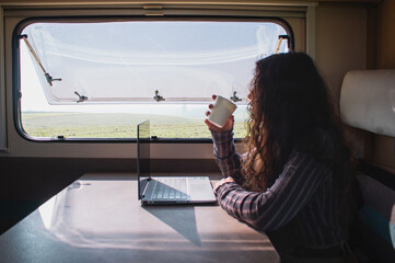 young woman work with her computer on her motor home drinking coffee.