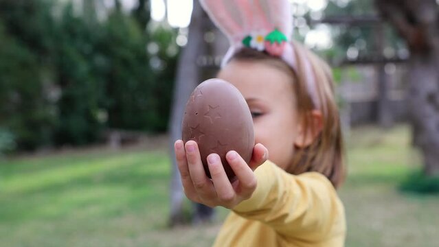 Easter egg hunt. Excited emotion kid girl in bunny ears rabbit costume hold Easter chocolate egg in garden outside. Children positive emotions. Child happy Easter