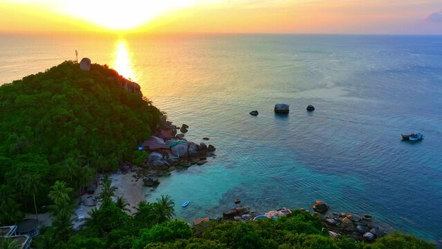 Sun-kissed shores with golden hues embrace a tropical coastline under the painted sky of sunset's embrace. Bird's eye view. Cinematic footage. Tao island, Surat Thani, Southern Thailand. 4K.
