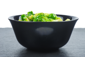 Cooked organic brussels sprouts in black bowl isolated on white background.