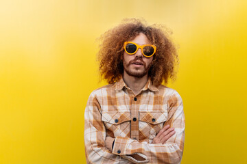 Man wearing sunglasses and standing with arms crossed in front of yellow wall