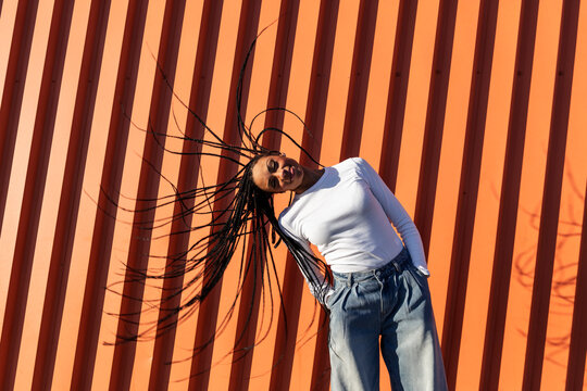 Smiling young woman tossing hair in front of wall