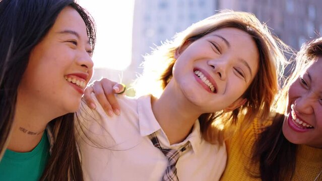 Three happy and joyful young Asian women embracing and looking laughing at camera outdoors. Group Chinese nice females friends having fun together sunny day. Generation z and positive relationships