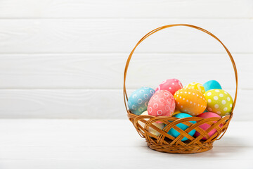 Easter basket filled with colorful eggs and a bouquet of tulips on a textured wooden table. Easter celebration concept. Colorful easter handmade decorated Easter eggs. Place for text. Copy space