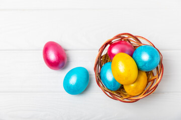 Easter basket filled with colorful eggs and a bouquet of tulips on a textured wooden table. Easter...