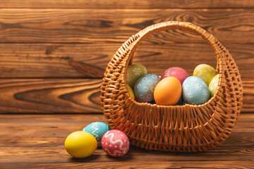 Easter basket filled with colorful eggs and a bouquet of tulips on a textured wooden table. Easter celebration concept. Colorful easter handmade decorated Easter eggs. Place for text. Copy space