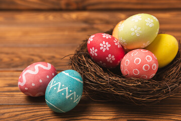 Colorful Easter eggs in a nest and a bouquet of tulips on a textured wooden table. Easter celebration concept. Colorful easter handmade decorated Easter eggs. Place for text. Copy space
