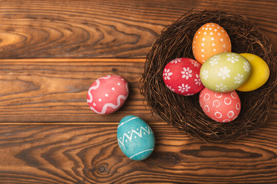 Colorful Easter eggs in a nest and a bouquet of tulips on a textured wooden table. Easter celebration concept. Colorful easter handmade decorated Easter eggs. Place for text. Copy space