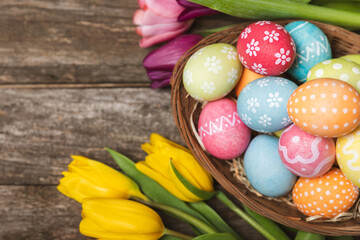 Obraz na płótnie Canvas Easter basket filled with colorful eggs and a bouquet of tulips on a textured wooden table. Easter celebration concept. Colorful easter handmade decorated Easter eggs. Place for text. Copy space