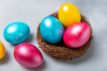 Colorful Easter eggs in a nest and a bouquet of tulips on a textured wooden table. Easter celebration concept. Colorful easter handmade decorated Easter eggs. Place for text. Copy space