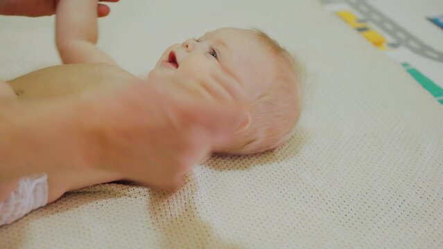 Cute Caucasian baby boy smiles during a massage. The massage therapist warms up the child body and arms. Physical development of infant age children.