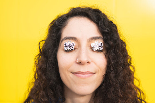 Smiling curly haired woman with butterfly stickers on eyes against yellow background