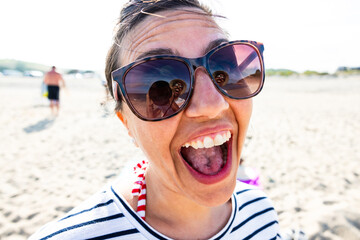 Joyful woman sticking out tongue on sunny beach day