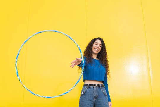 Smiling woman playing with hula hoop against yellow background