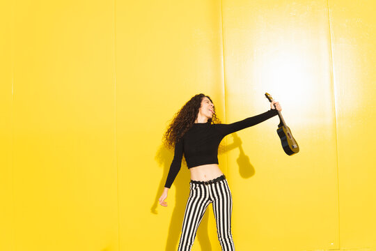 Passionate woman holding ukulele against yellow background