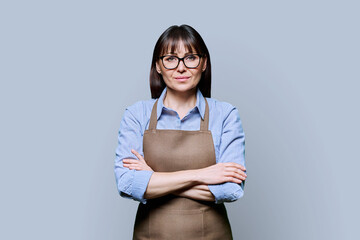 Confident serious middle-aged woman in apron on gray background