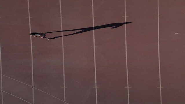 Aerial image over an athletics track where a boxer is warming up and practicing shadow, the long shadow produced by the sunrise sun offers a captivating image.