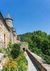 Fototapeta na wymiar Inner courtyard of the monastery. Stone wall and dome of church, trees and flowers. Tower on the hill.