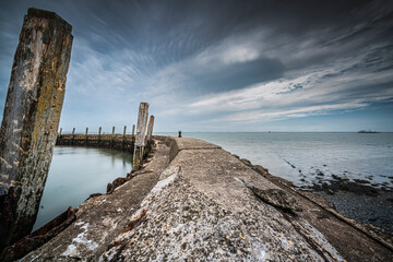 Dilapidated mooring quay in a round shape of weathered concrete with a view of the sea and a threatening cloudy sky above - 746436964