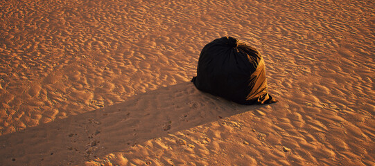 Black garbage bag left on tropical beach with rippled sand. Golden hour sunlight. - 746436974
